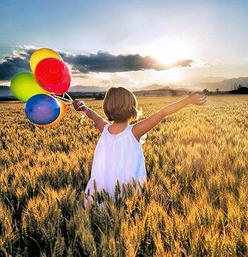 Young girl with her arms raised, holding balloons, in a wheatfield.