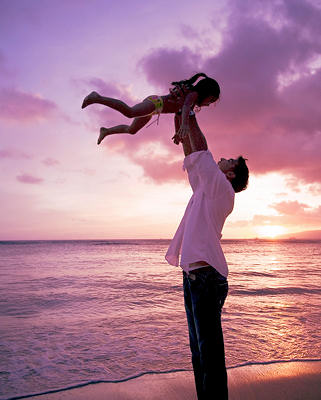 Man lifting young girl in the air, by the ocean, during an afternoon sunset.