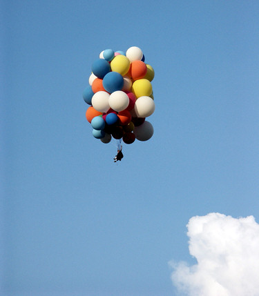 Man in a lawn chair hanging from a bunch of balloons up in the sky.