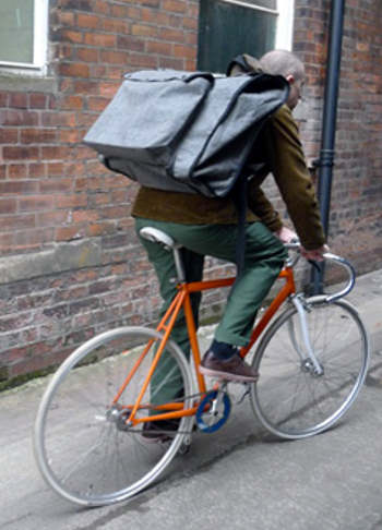 Man on a bicycle with a large shoulder bag on his back.