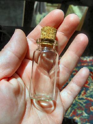 A hand holding a small bottle with a cork in the top.