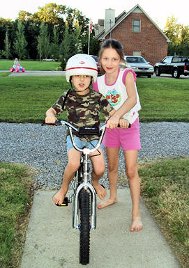 Young girl helping her younger brother learn to ride a bike.