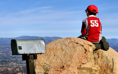 Boy sitting on a rock by the mailbox, gazing out across the valley.