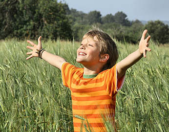 Young boy in a field, arms raised, praising.