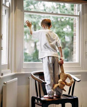 Young boy looking out the window and holding a stuffed animal.