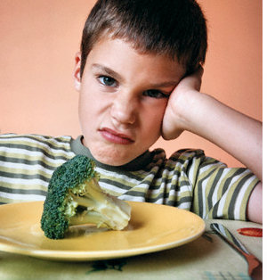 Young boy, with a discussed look on his face, staring at broccoli on his plate.