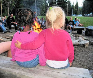 People around a campfire - one little girl has her arm aound the back of her little friend.