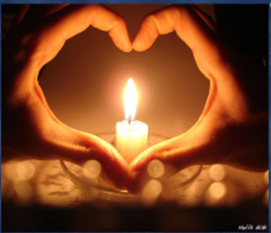Hands shaped like a heart around a candel.