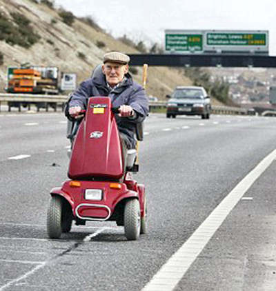 Senior citizen driving his little battery powered cart down the freeway in the left lane.'