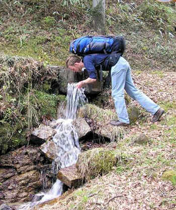 Man stooping down to drink from a mountain spring.