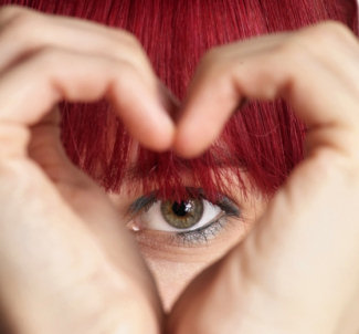 Eyeball looking through hands shaped like a heart.