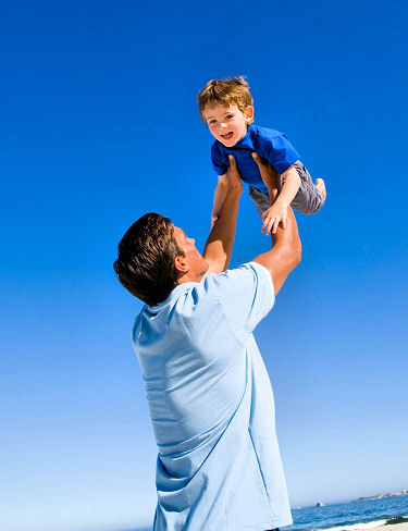 Father tossing his son in the air at the beach.