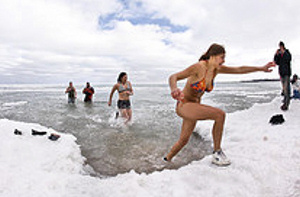 Female swimmer coming out of freezing water and stepping on a snowbank.