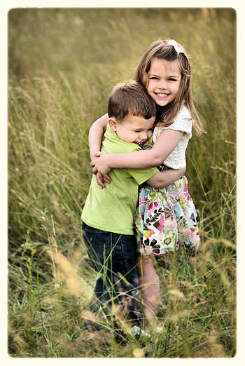 Young girl hugging her little brother in a field.