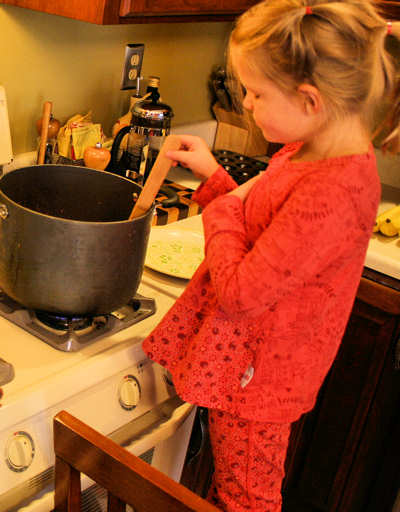 Young girl standing on a chair, at the stove, cooking her great-grandmothers spaghetti sauce.