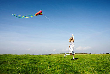 Young girl running with a kite in an open field.