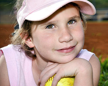 Sweet looking young girl with cap holding a softball.