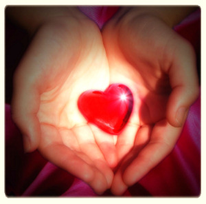 Two open hands holding a small red heart - symbolizes the gift of love for others.