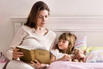 Mother reading the bible to her young daughter in bed.