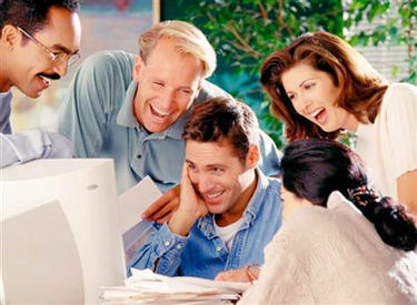 Five office workers standing around a computer monitor laughing.