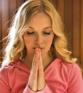 Young woman, eyes closed, hands folded, head bowed, in prayer.