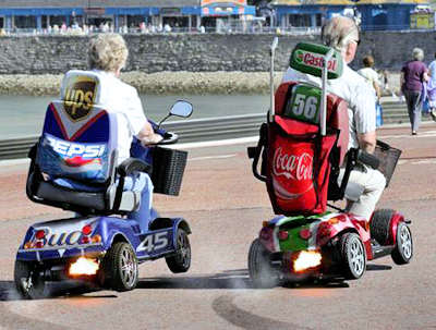 Two senior citizens out having fun, racing their 4-wheel powered scooters.