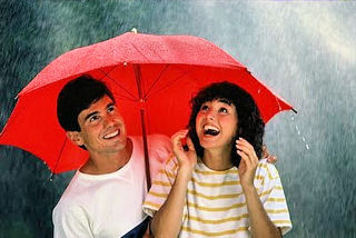 Young man and woman holding a red umbrella in the rain.