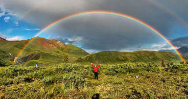 Rainbow with man raising his arms to the sky.