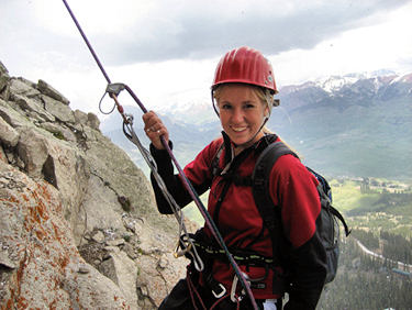 Young woman rappelling down the side of a step cliff.
