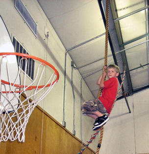 Boy climbing a rope in the gym.