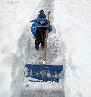 Little boy with snow shovel in deep snow.