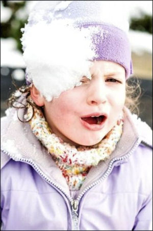 Young boy getting hit in the face with a snowball.