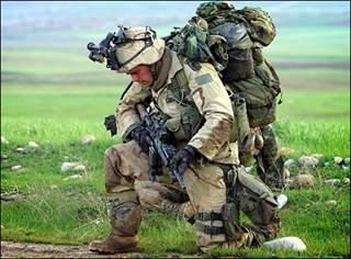 A soldier, in full battle gear, praying.