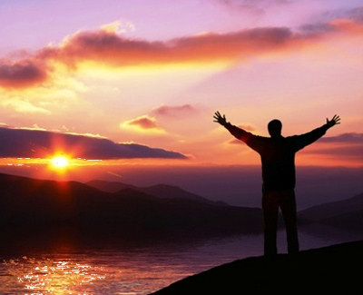 Man with arms lifted up looking at a beautiful sunset and giving praise to God.