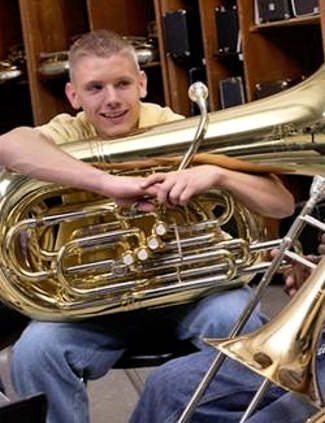 A smiling teenage boy with a tuba on his lap.