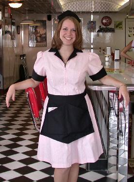 Waitress in a pink dress standing by a counter.