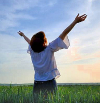 Young woman in a field with her hands raised in praise.