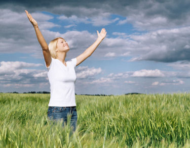 Woman standing in a field with her arms raised, giving thanks.