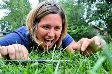 Woman snipping grass lawn, one blade at a time, with sewing scissors.