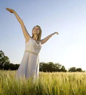 Happy woman, standing in a field, with her arms raised in praise.