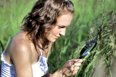 Woman using a magnifying glass to look at some grass.
