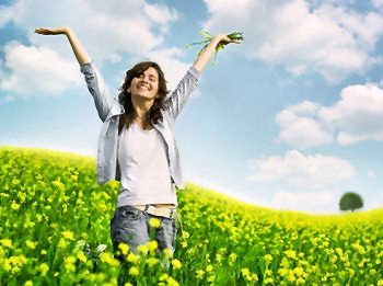 Woman standing in a field of yellow flowers, smiling with arms raised high, enjoying the new day.