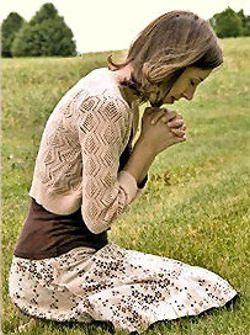 Young woman sitting on the grass and praying in the park.